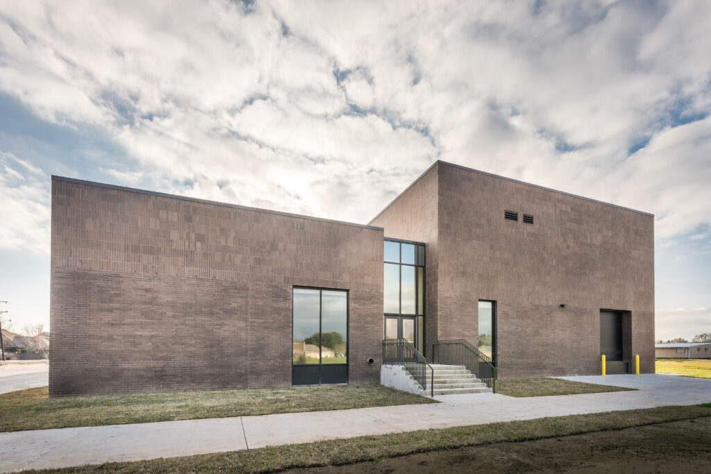 Front exterior of Comeaux High School Performing Arts Academy dark brick with rectangular windows under dramatic clouds